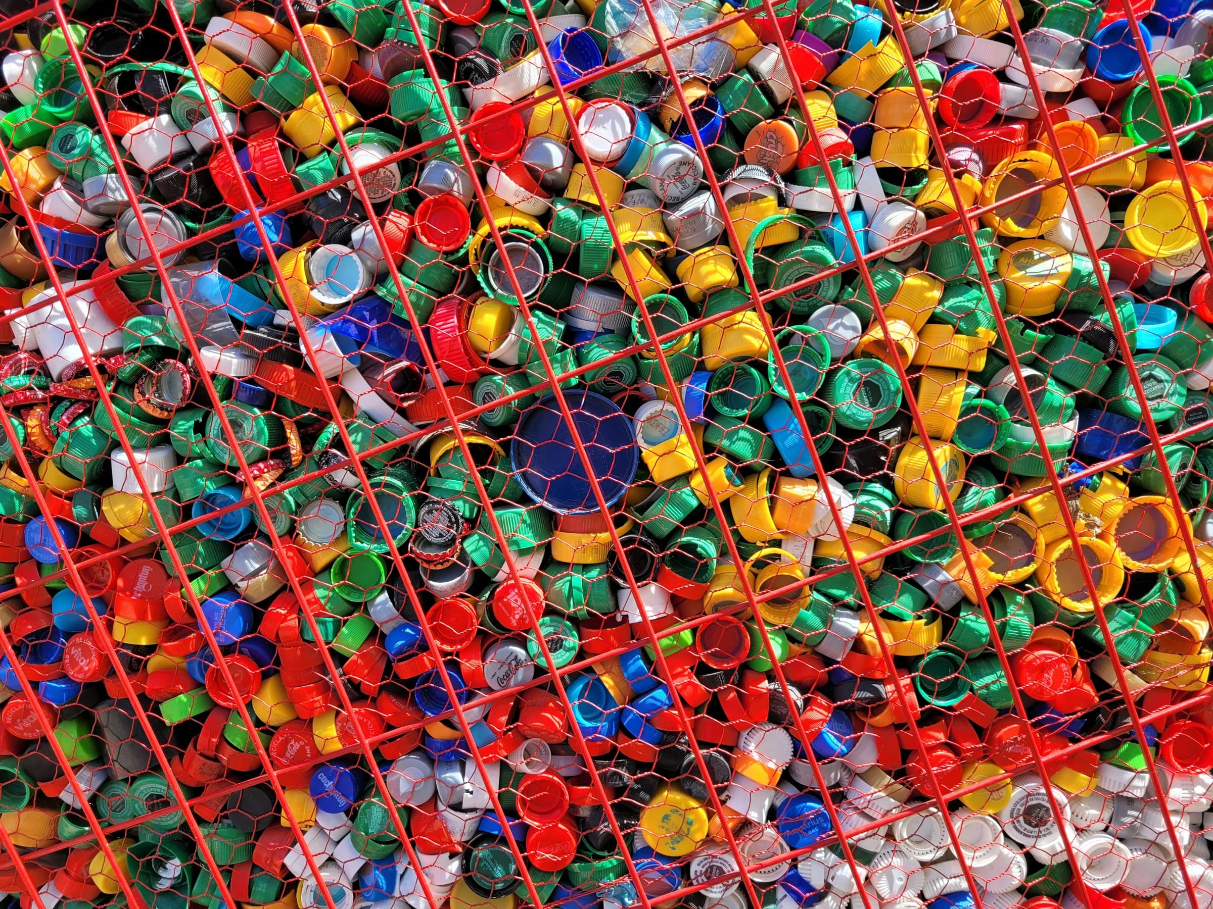 Collected bottle caps behind a recycling collection cage